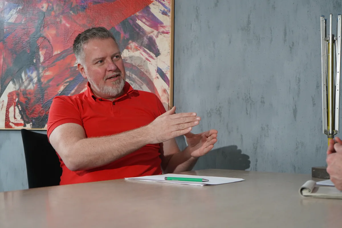 Ein bärtiger Mann in rotem Polo-Shirt an einem Sitzungstisch.