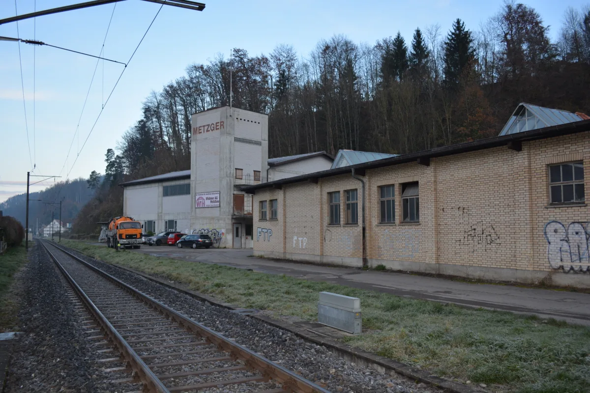 Man sieht ein brach liegendes Industrieareal mit parkierten Autos und stillgelegten Gebäuden.