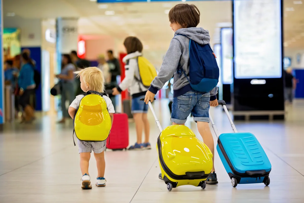 Mit der ETI-Familienversion sind alle, die mit dem Inhaber des ETI-Schutzbriefes im selben Haushalt wohnen, automatisch mitversichert. Zwei Brüder an einem Flughafen, mit Koffern unterwegs.