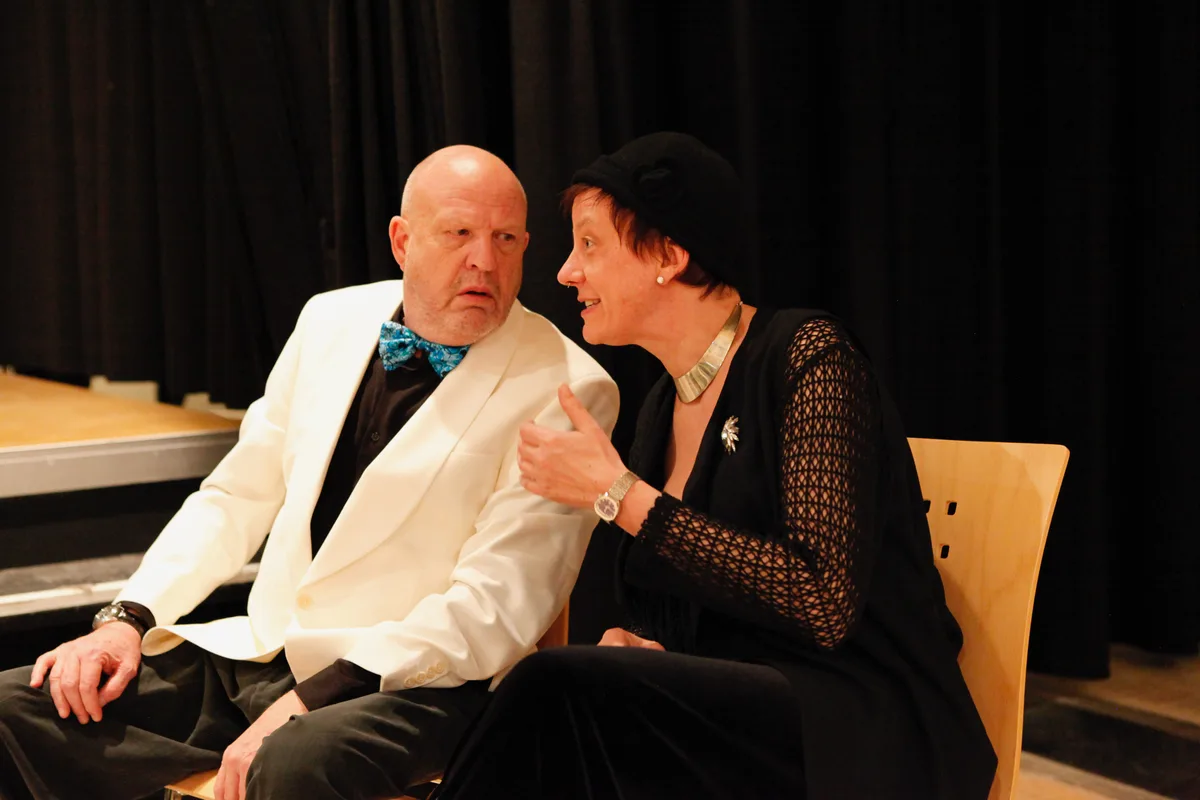 Ein Mann und eine Frau sprechen abseits einer Theaterbühne miteinander.