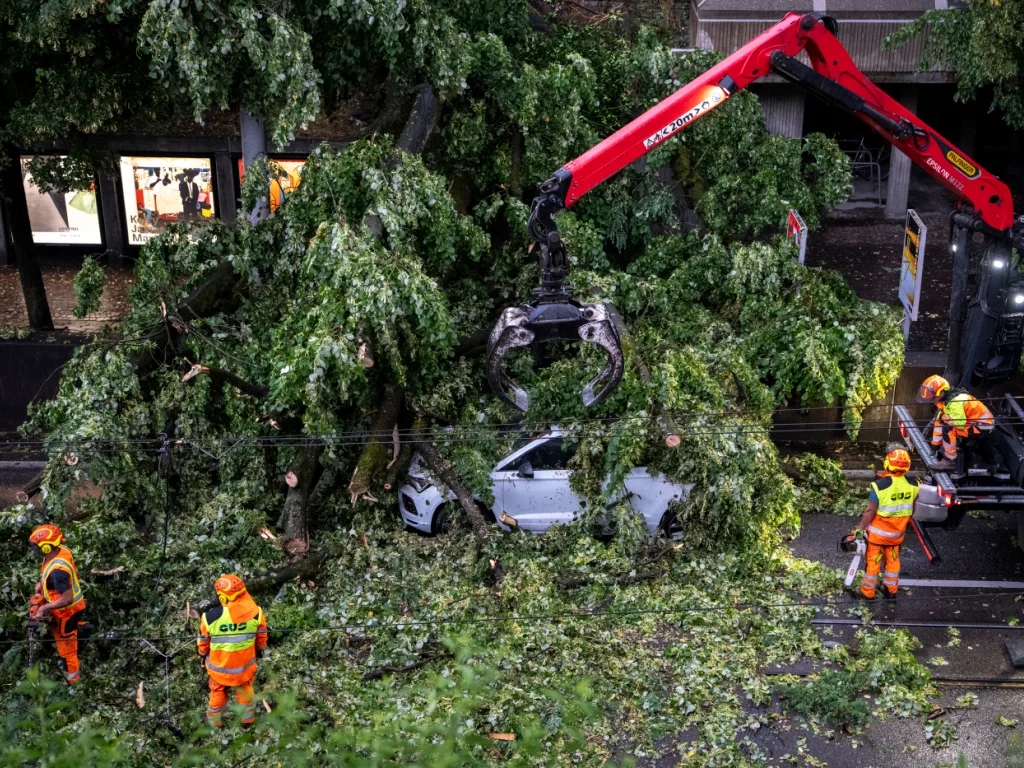 Helfer bergen am Freitag ein Auto unter dem umgestürzten Baum an der Rämistrasse in Zürich, der nach einem Blitzeinschlag drei Autos und die Fahrleitung der VBZ getroffen hat. Helfer bergen am Freitag ein Auto unter dem umgestürzten Baum an der Rämistrasse in Zürich, der nach einem Blitzeinschlag drei Autos und die Fahrleitung der VBZ getroffen hat.