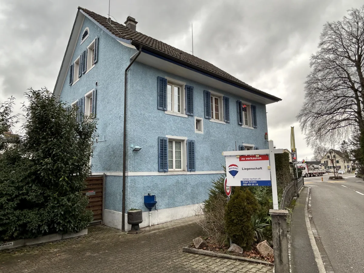 Ein blaues Haus in Pfäffikon mit einem Verkaufsschild davor.