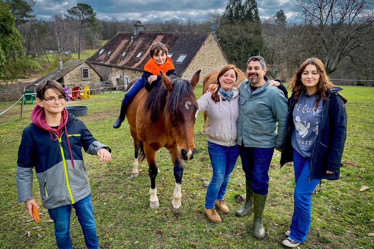 Jetzt lebt die Familie in Frankreich auf einem grossen Grundstück. Man sieht eine Familie mit drei Kindern. Ein Kind sitzt auf einem braunen Pferd.