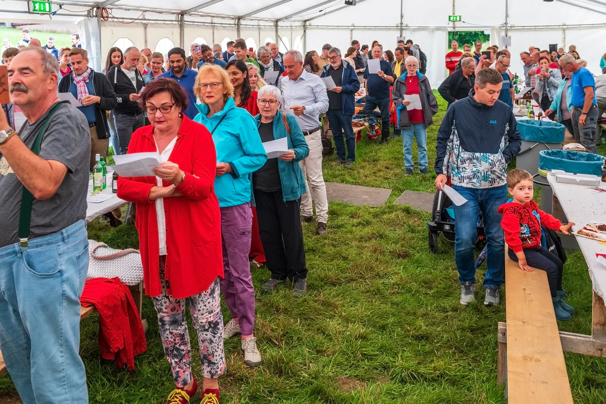 Viele Leute singen in einem Festzelt ein Lied.