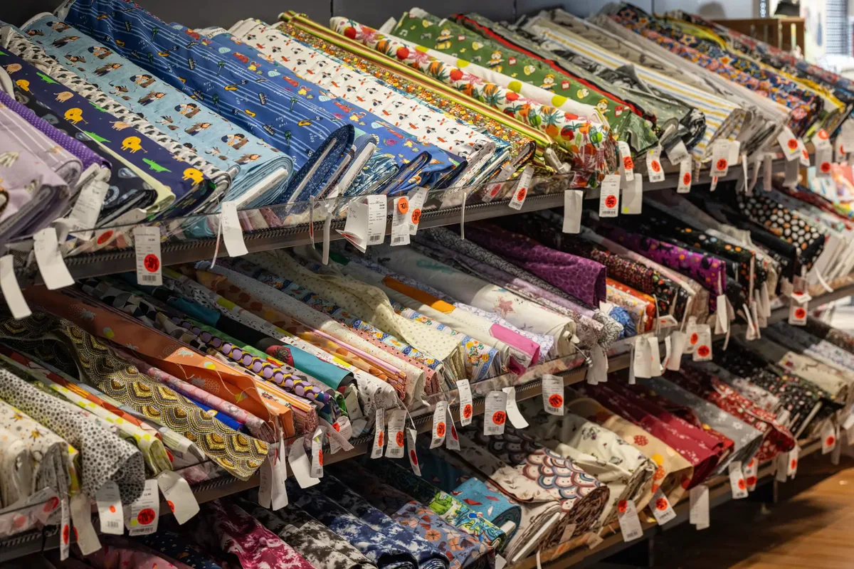 Orange Punkte zeigen die Preisreduktionen auf den verschiedenen Stoffen beim Räumungsverkauf in Wädenswil. Viele verschiedenfarbige Stoffball in Regalen.