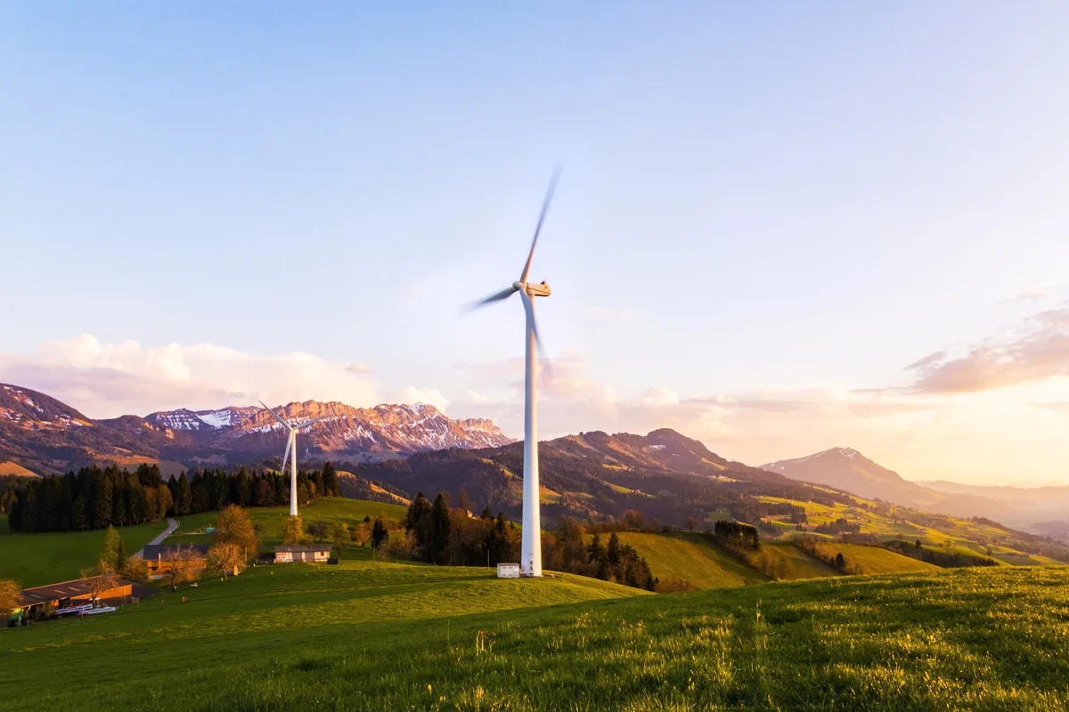 Zwei Windräder vor einer Bergkulisse in der Schweiz.